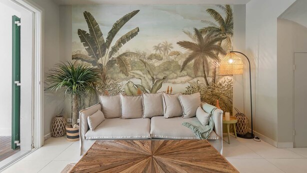 A living room with a sofa, a coffee table, a floor lamp, and a mural of tropical foliage. - Maison GAMA, 2 bedrooms and shared pool (CISTERN!!!) (Collectivity of Saint Martin)