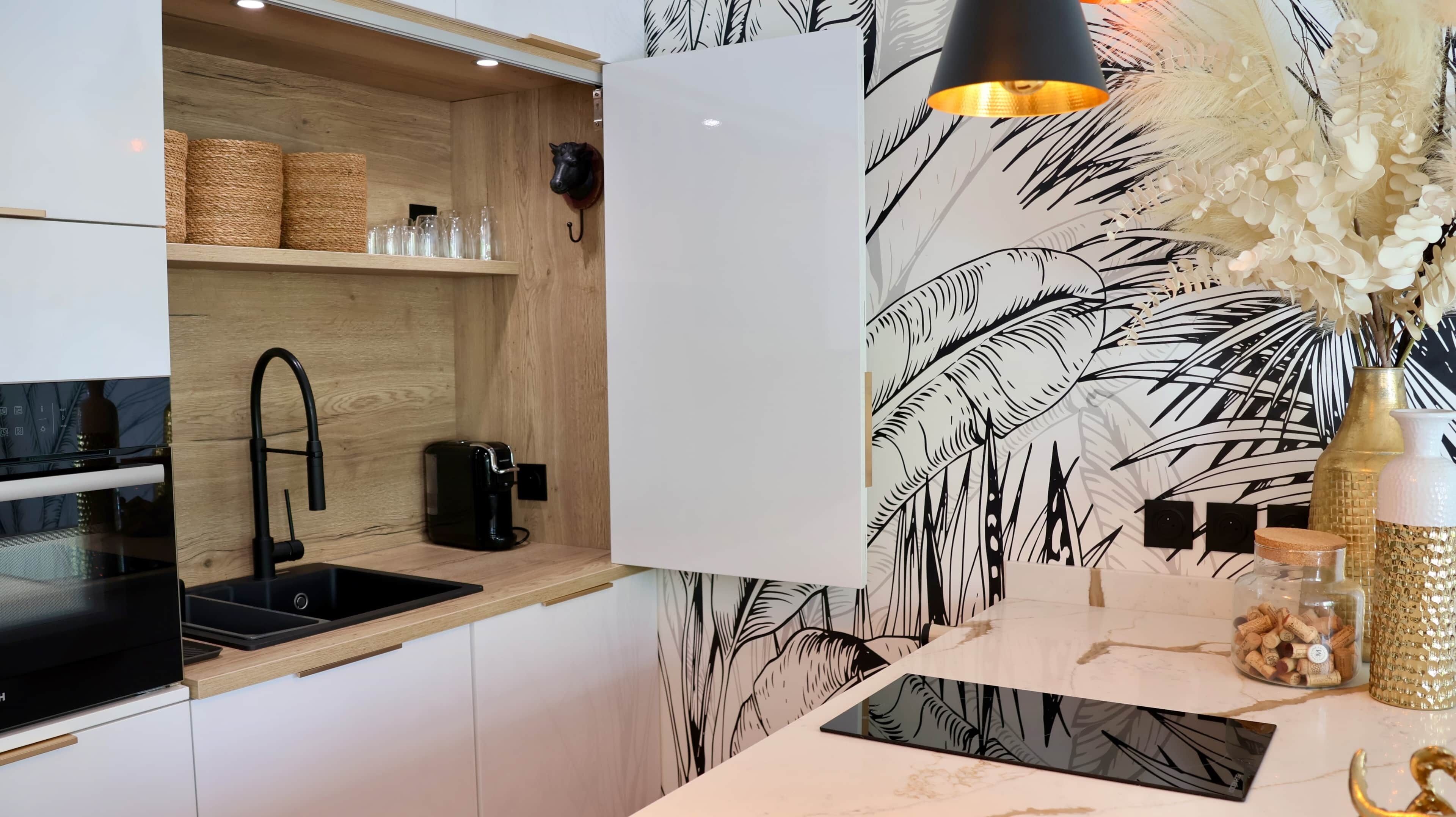 Une cuisine moderne avec une étagère en bois, une machine à café noire et un mur décoratif orné d’un motif de feuilles.