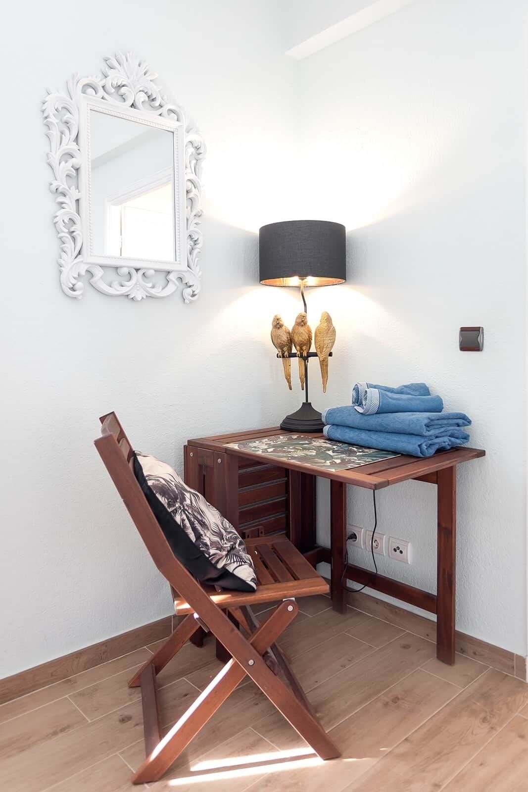 Una habitación con un escritorio de madera, una silla, una lámpara y un espejo.