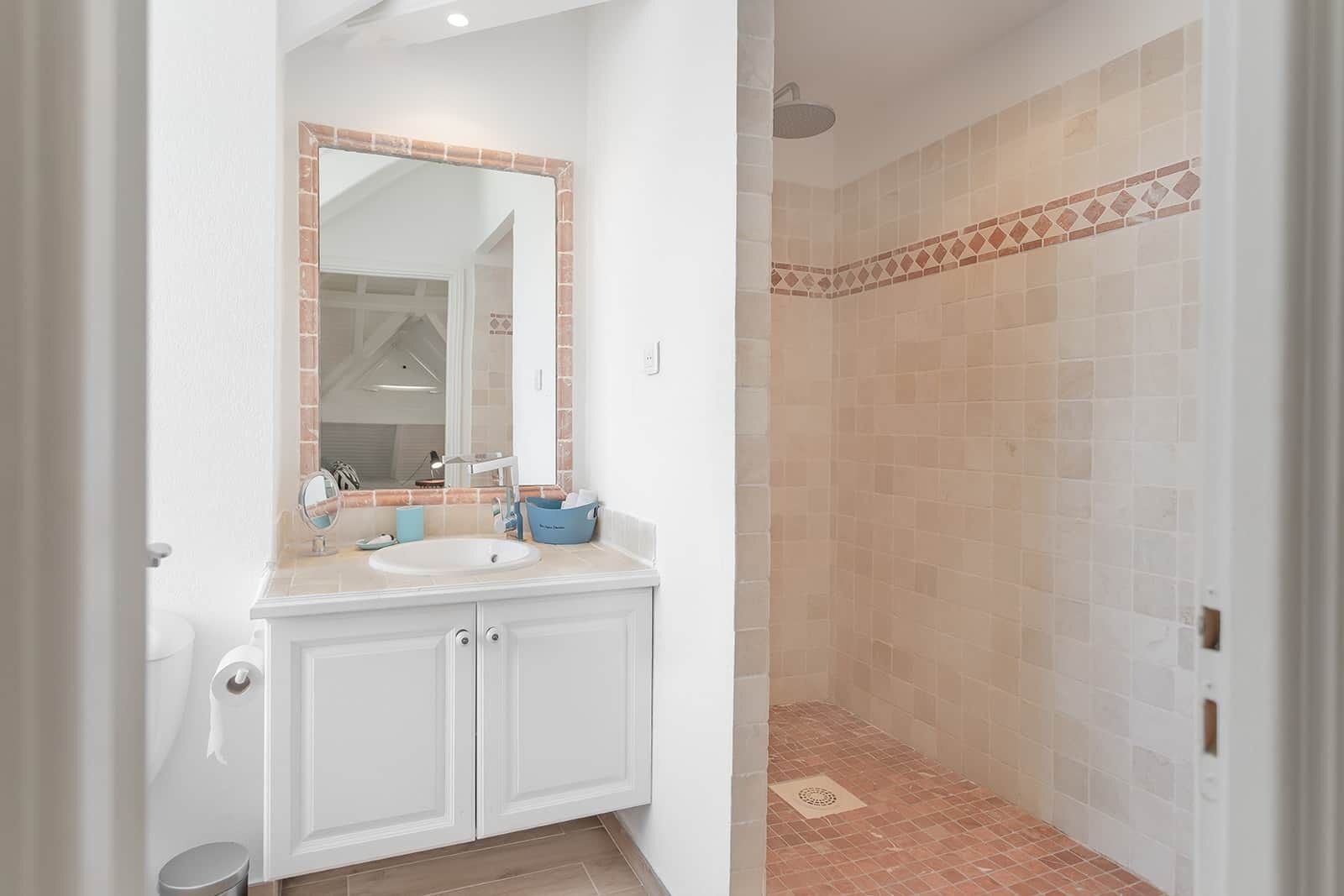 Ein Badezimmer mit weißem Waschtisch, einem Spiegel mit braunem Rahmen und einer Duschkabine mit gemusterten Fliesen.