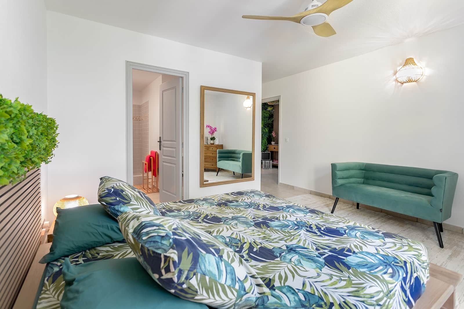 Un dormitorio con una cama, un sofá verde, un espejo y un ventilador de techo.