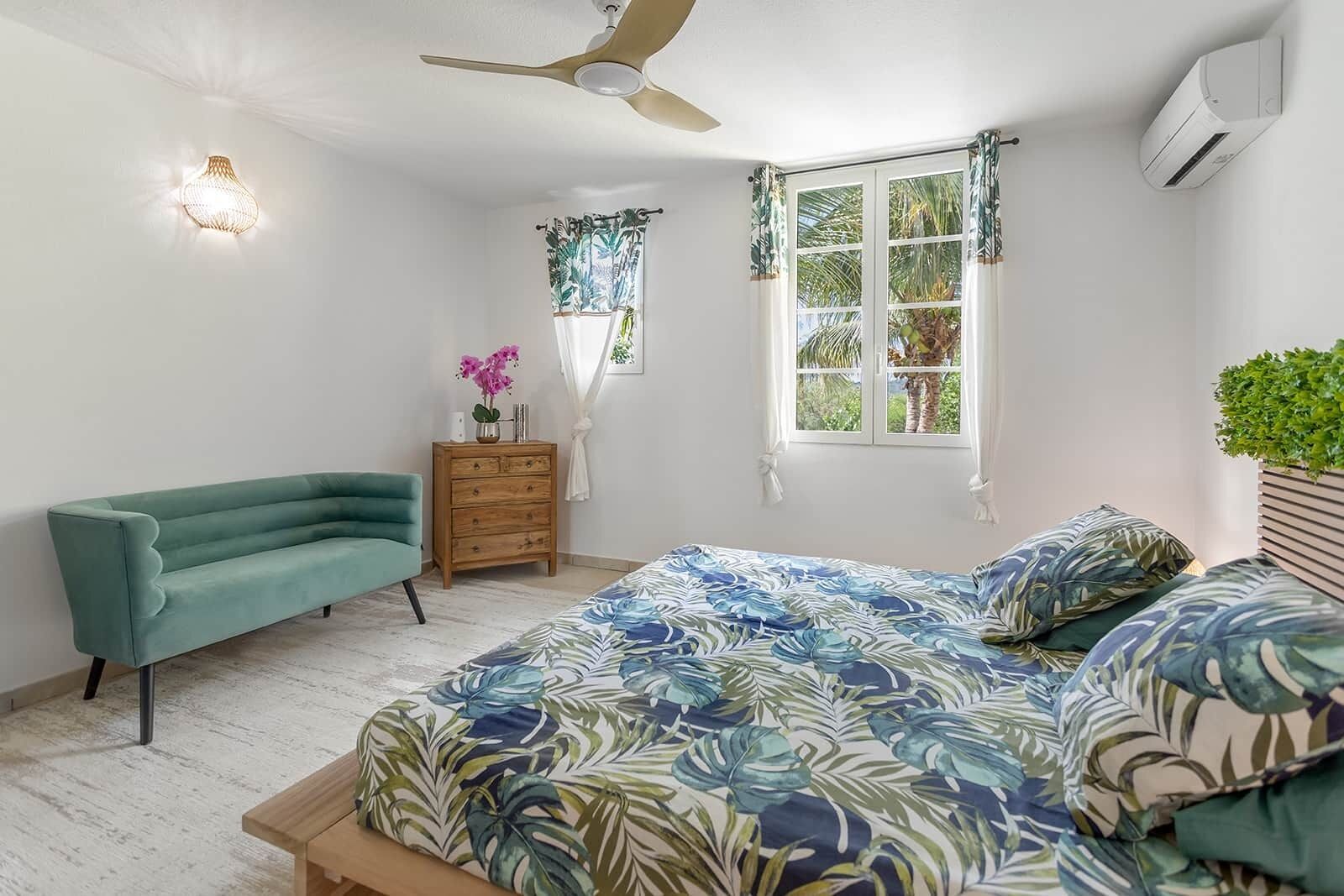 A bedroom with a bed, a sofa, a dresser, a ceiling fan, and a window with curtains.