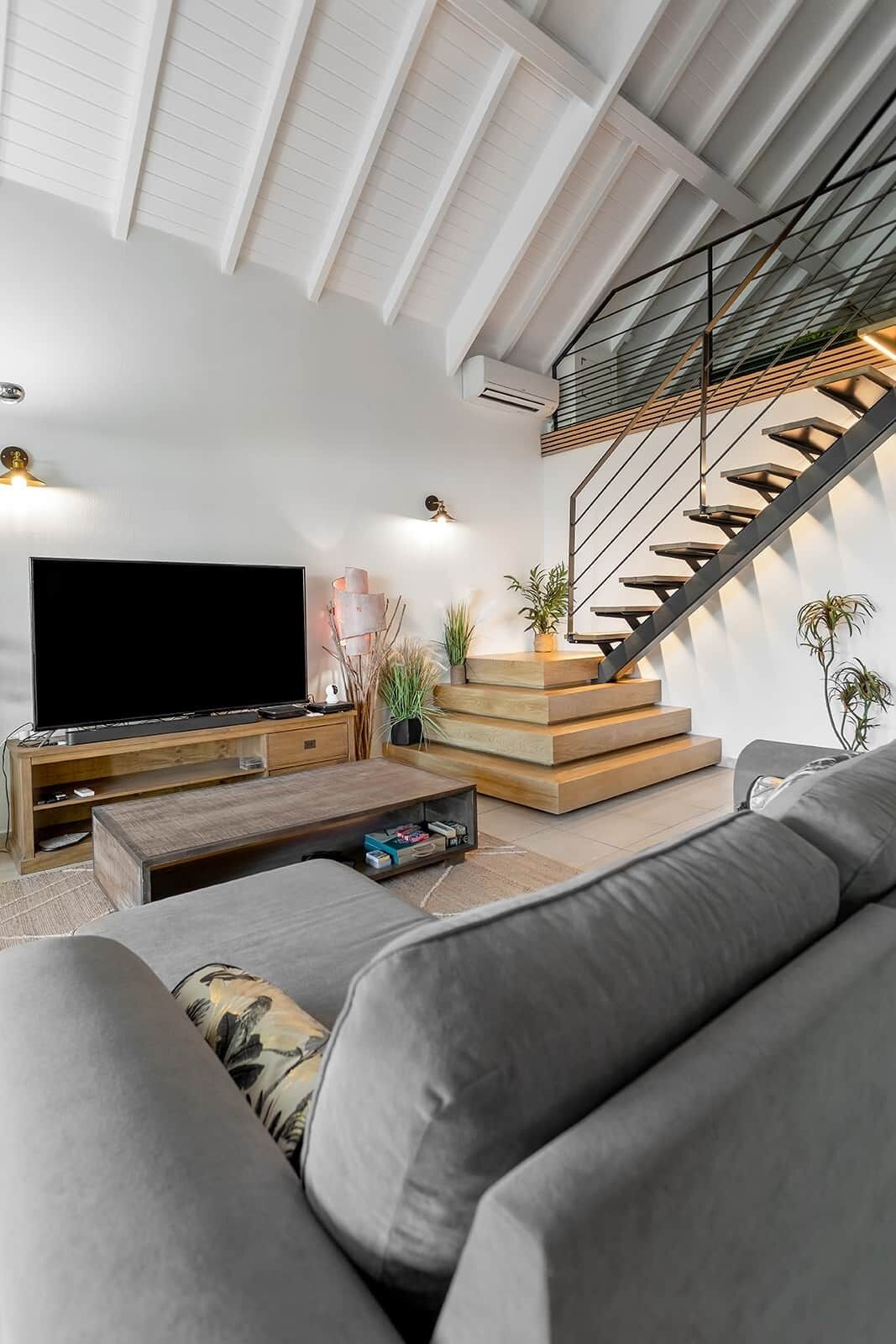 Un salon moderne avec un téléviseur à écran plat, une table basse en bois et un canapé gris.