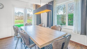 Ein Essbereich mit Holztisch und Stühlen, großen Fenstern mit Vorhängen und einer Hängelampe.