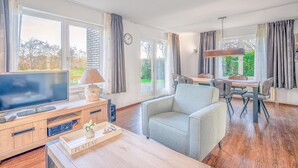 Ein modernes Wohnzimmer mit Flachbildfernseher, einer Holz-Unterhaltungseinheit und einem Essbereich mit Tisch und Stühlen.