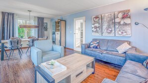 Ein modernes Wohnzimmer mit einer Couch, Sesseln, einem Couchtisch und einem Essbereich mit Stühlen und Tisch.