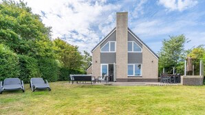 Ein modernes, zweistöckiges Haus mit Backsteinfassade, einer großen Veranda und einem gepflegten Rasen.