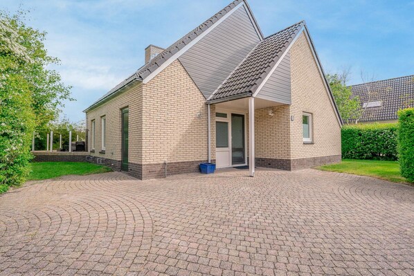Une maison à deux étages avec un toit en pente, un porche couvert et une allée pavée.
