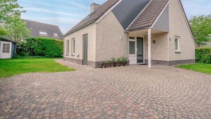 A two-story house with a brick exterior, a sloped roof, and a paved driveway. - Charming Villa Near the sea and Forest (De Koog)