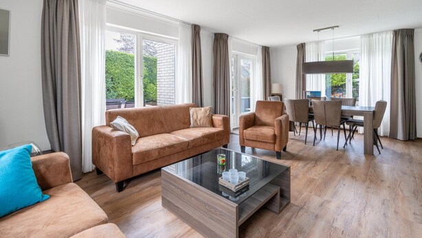 A modern living room with a sofa, armchair, and coffee table. There is a dining area with a table and chairs. - Charming Villa Near the sea and Forest (De Koog)