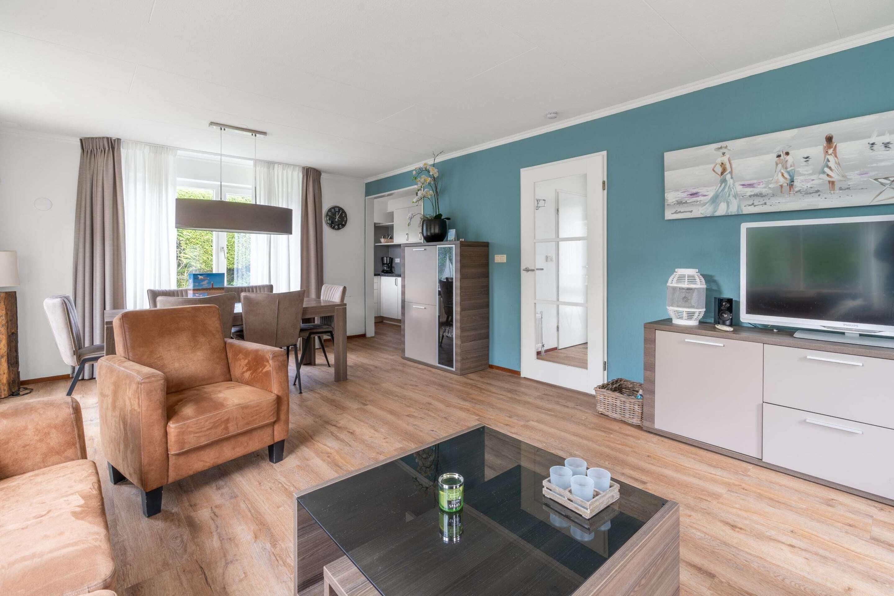 A modern living room with a sofa, a coffee table, and a TV. There is a kitchen area with cabinets and a refrigerator.