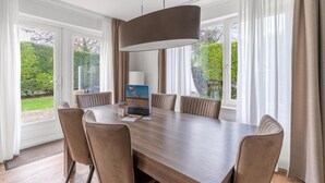 A modern dining area with a large table, six chairs, and a hanging light fixture. - Charming Villa Near the sea and Forest (De Koog)