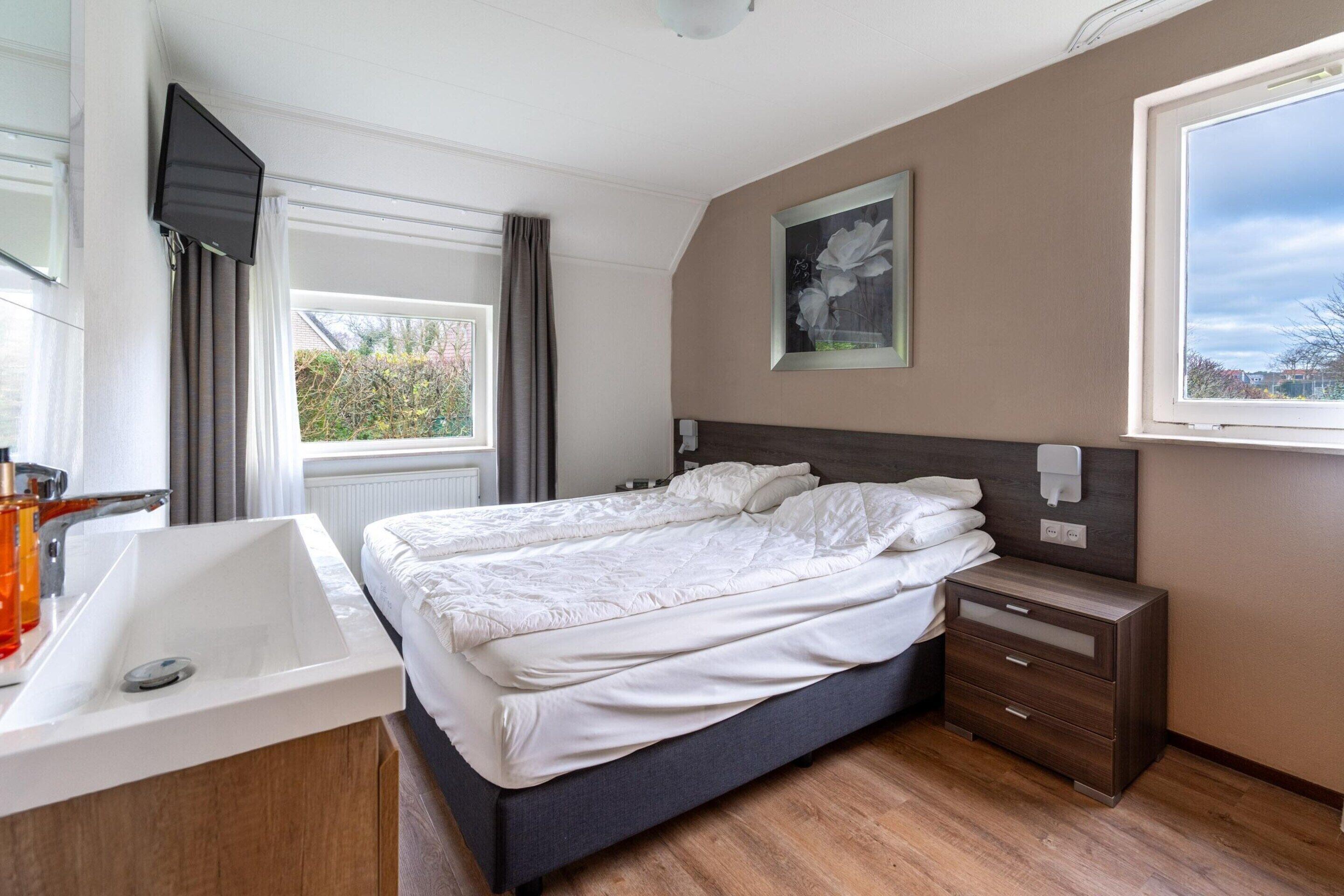 A bedroom with a bed, bedside tables, a TV, and a window.