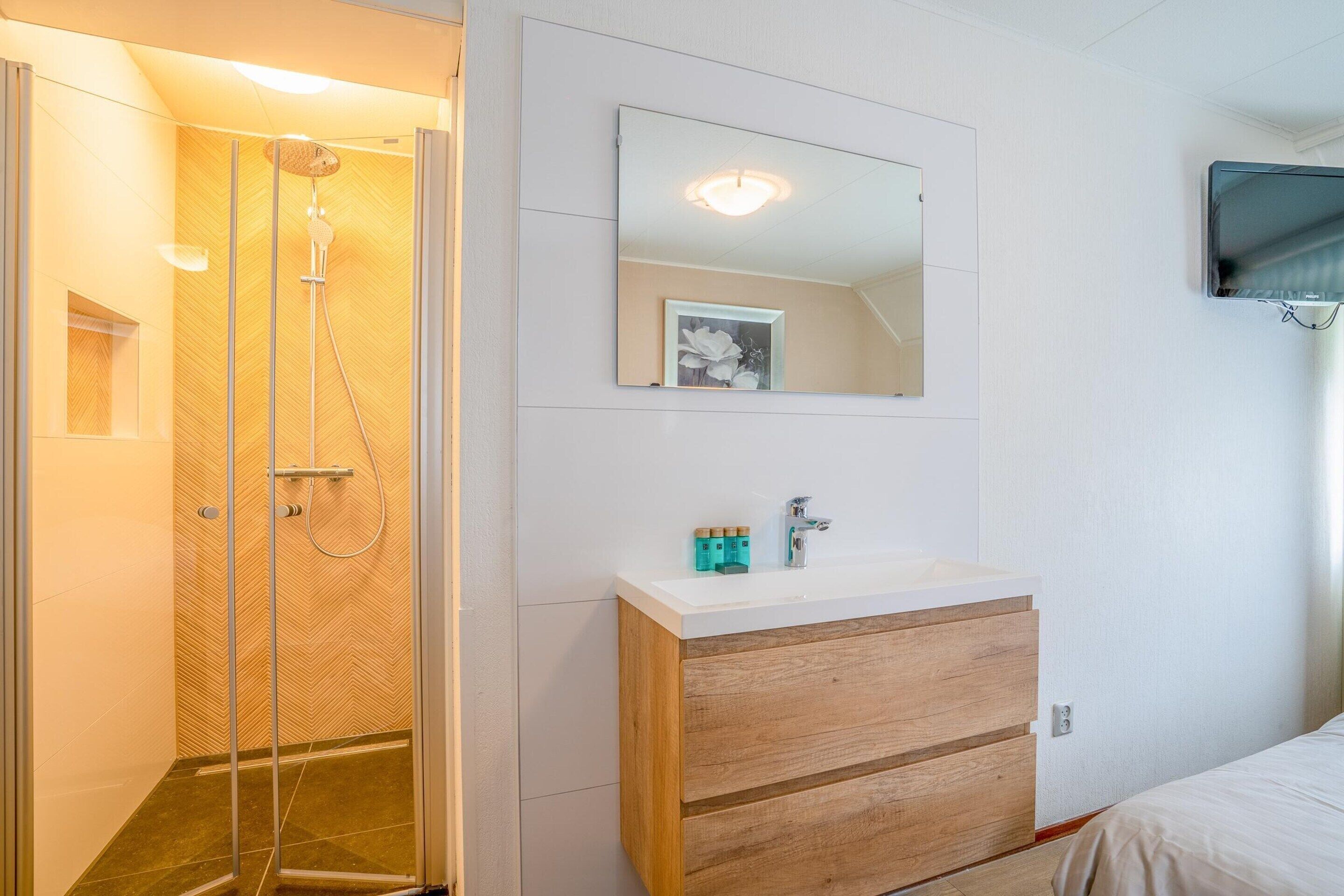 Un bagno con doccia, lavabo con specchio e televisore a parete.