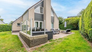 A two-story house with a brick exterior, a chimney, and a patio with outdoor furniture. - Charming Villa Near the sea and Forest (De Koog)