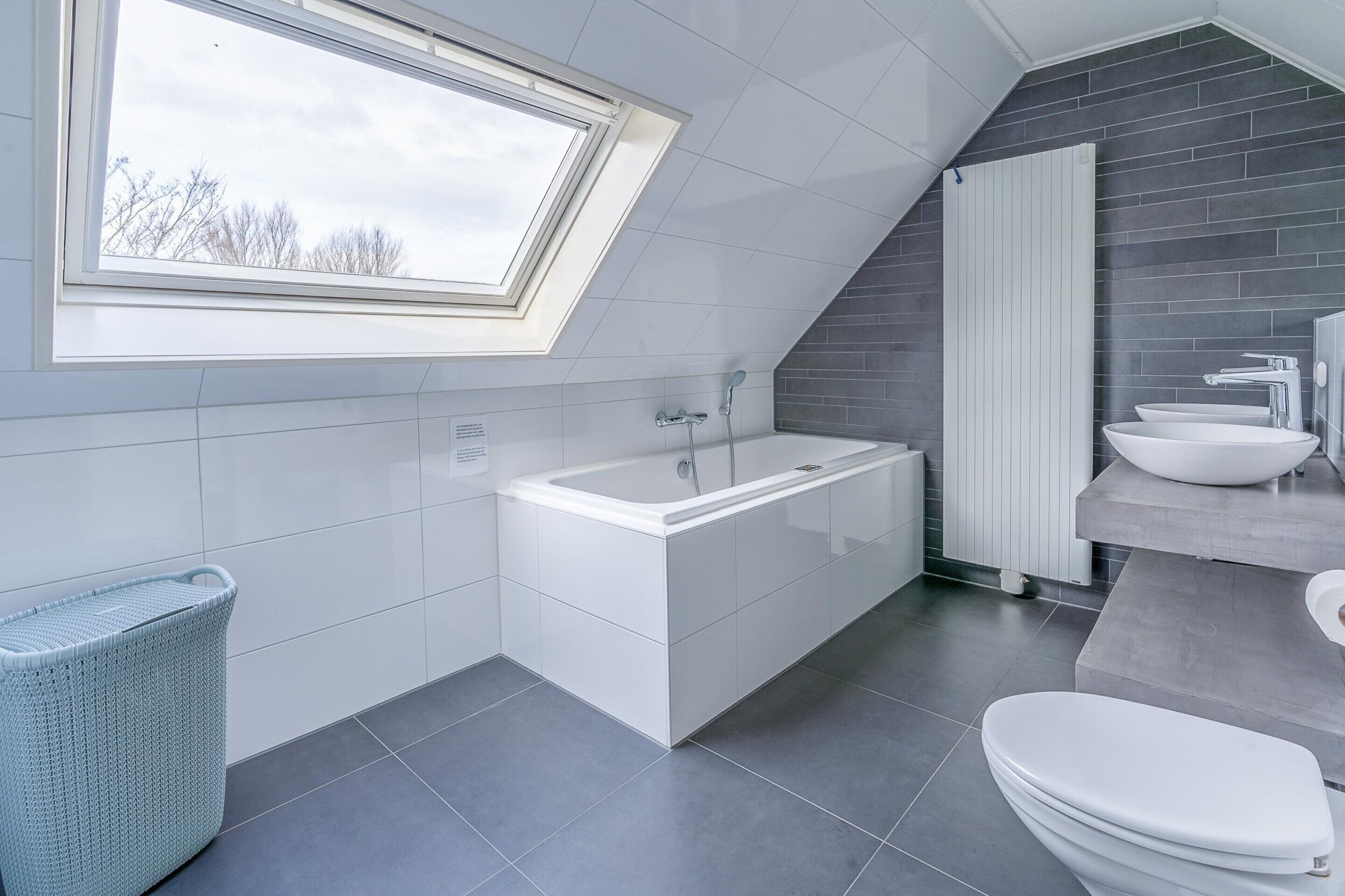 A modern bathroom with a skylight, a bathtub, a sink, and a toilet.