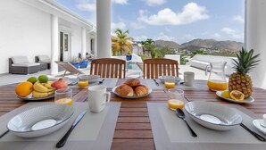 A breakfast table set with fruits, croissants, and orange juice on a terrace with a view of mountains and a pool. - Villa Mallory, 3 bedrooms, private pool and ocean view (Collectivity of Saint Martin)