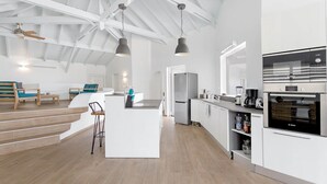 A modern kitchen with white cabinetry, a Bosch oven, and a central island with bar stools. - Villa Mallory, 3 bedrooms, private pool and ocean view (Collectivity of Saint Martin)