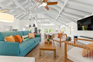 A spacious living area with a high ceiling, a ceiling fan, a sofa with cushions, a coffee table, and a television mounted on the wall.