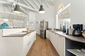 A modern kitchen with a stainless steel refrigerator, a coffee machine, and a large window providing natural light.