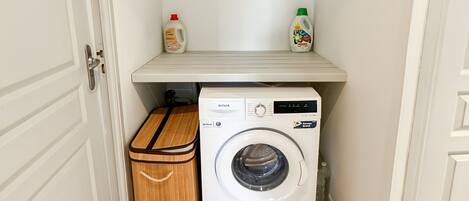 Ein kleiner Hauswirtschaftsraum mit Waschmaschine, Wäscheständer und einem Regal mit Waschmittel.