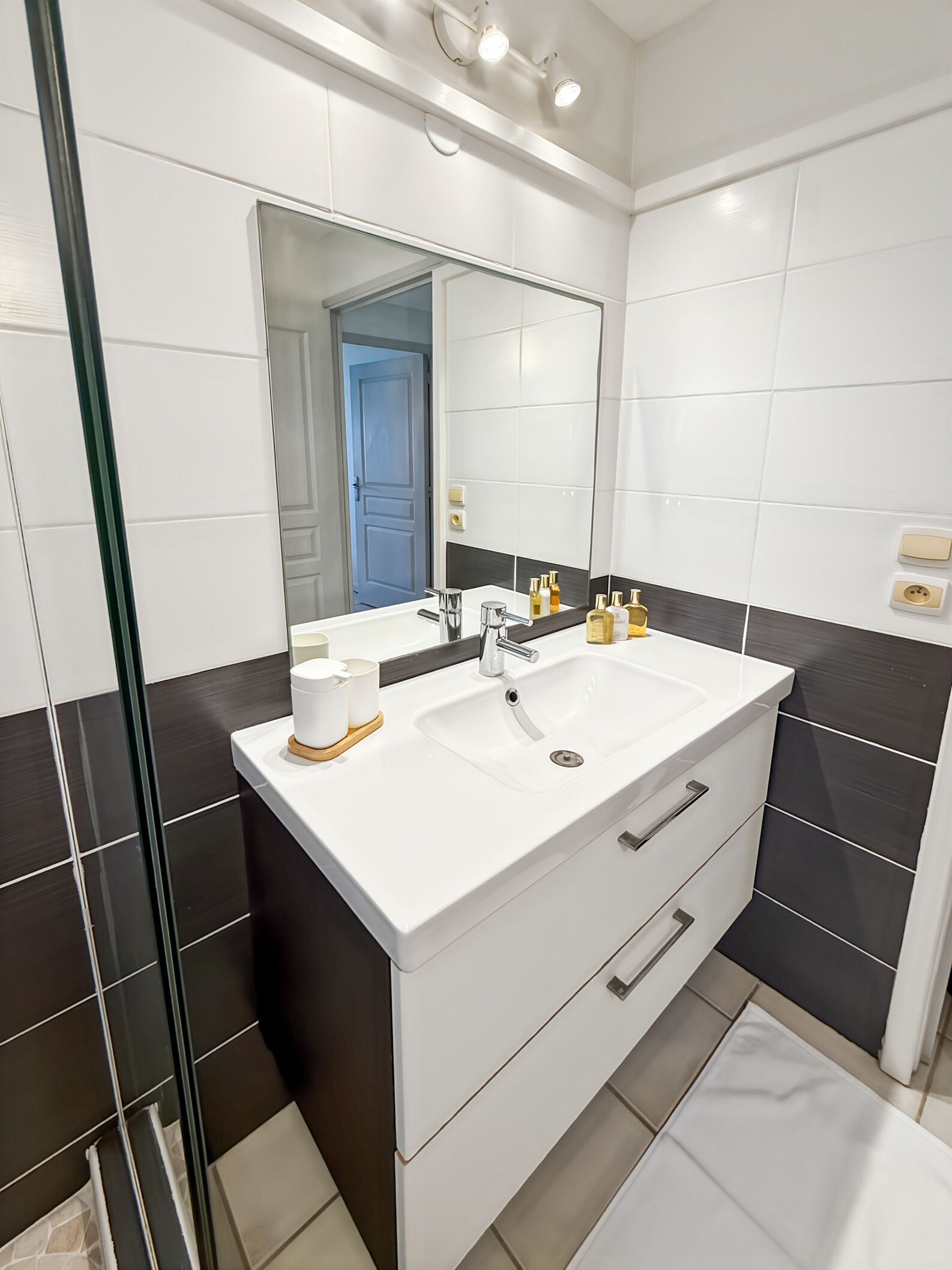 A modern bathroom with a white vanity, a large mirror, and a glass shower enclosure.