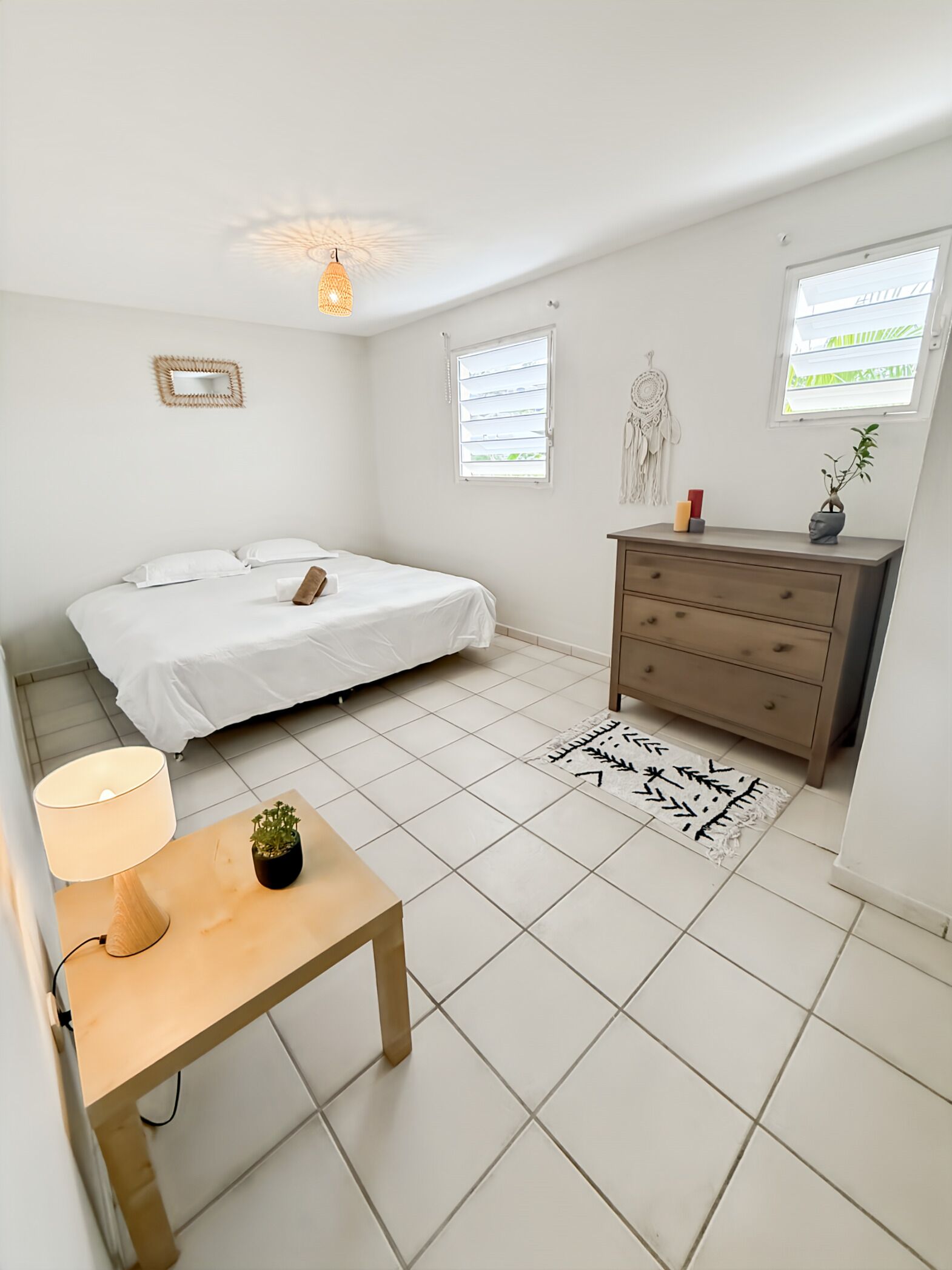 A minimalist bedroom with a bed, bedside table, lamp, dresser, and a rug.