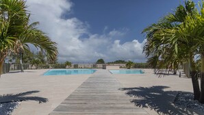 A pool area with two rectangular pools, a wooden walkway, and palm trees.