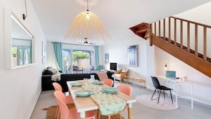 A modern living room with a dining area, a staircase, and a view of the outdoors.