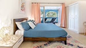 A bedroom with a bed, a nightstand, a chair, a balcony with a view, and a door.