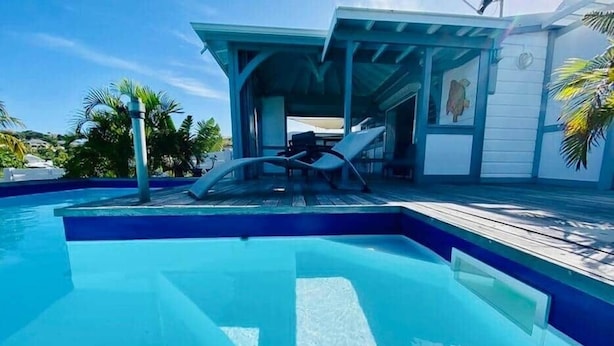 Una piscina con cubierta de madera, una zona de estar techada y un edificio con un mural.