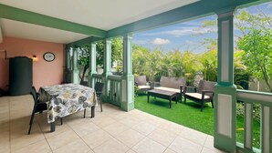 Une terrasse couverte avec une table et des chaises, entourée de rampes vertes et offrant une vue sur une végétation luxuriante.