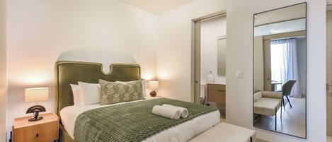 Habitación de hotel moderna con una cama grande, una mesita de noche con lámpara, un espejo y vistas a un balcón.