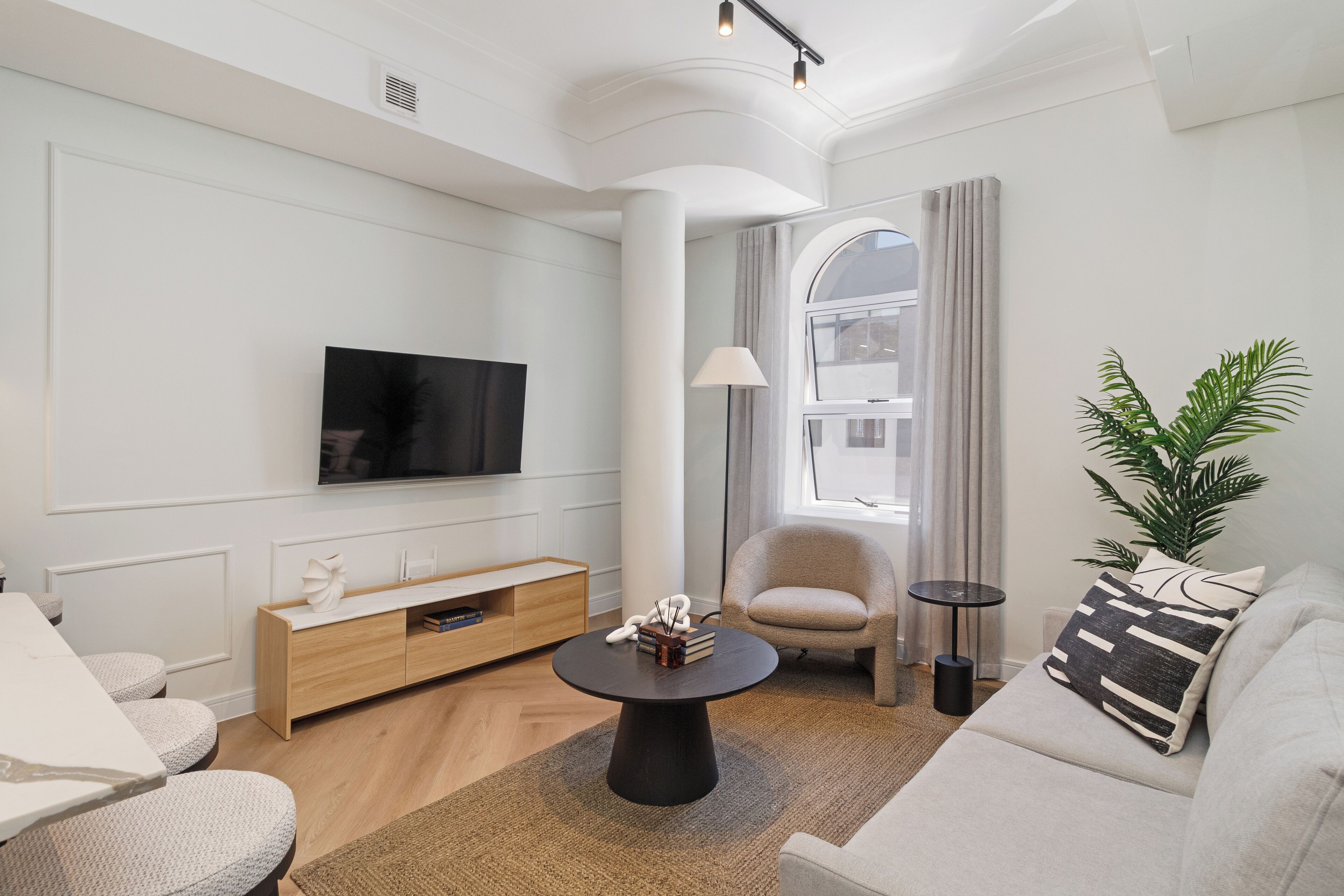 A modern living room with a flat-screen TV, a round coffee table, a sofa, a chair, and a potted plant.