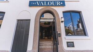 Das Hotel The Valour mit einer markanten Fassade, einem Schild und Blick auf die Stadtlandschaft durch die Fenster.