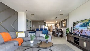 A modern living room with a grey sofa, two coffee tables, and a large flat-screen TV.