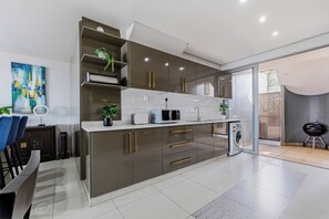 A modern kitchen with built-in appliances, a dining area with chairs, and a view to the outside. - Simbithi Coastal Escape | Luxury with Ocean Views (Dolphin Coast)
