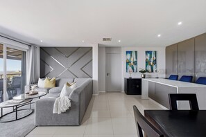 A modern living room with a grey sofa, a coffee table, and a dining area with a black table. - Simbithi Coastal Escape | Luxury with Ocean Views (Dolphin Coast)