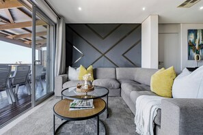 Una sala de estar moderna con un sofá seccional gris, una mesa de centro redonda y un amplio ventanal que ofrece vistas al exterior.
