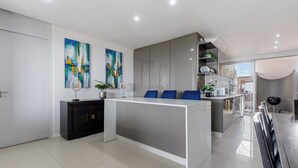 A modern kitchen with a central island, grey cabinets, and two abstract paintings on the wall. - Simbithi Coastal Escape | Luxury with Ocean Views (Dolphin Coast)