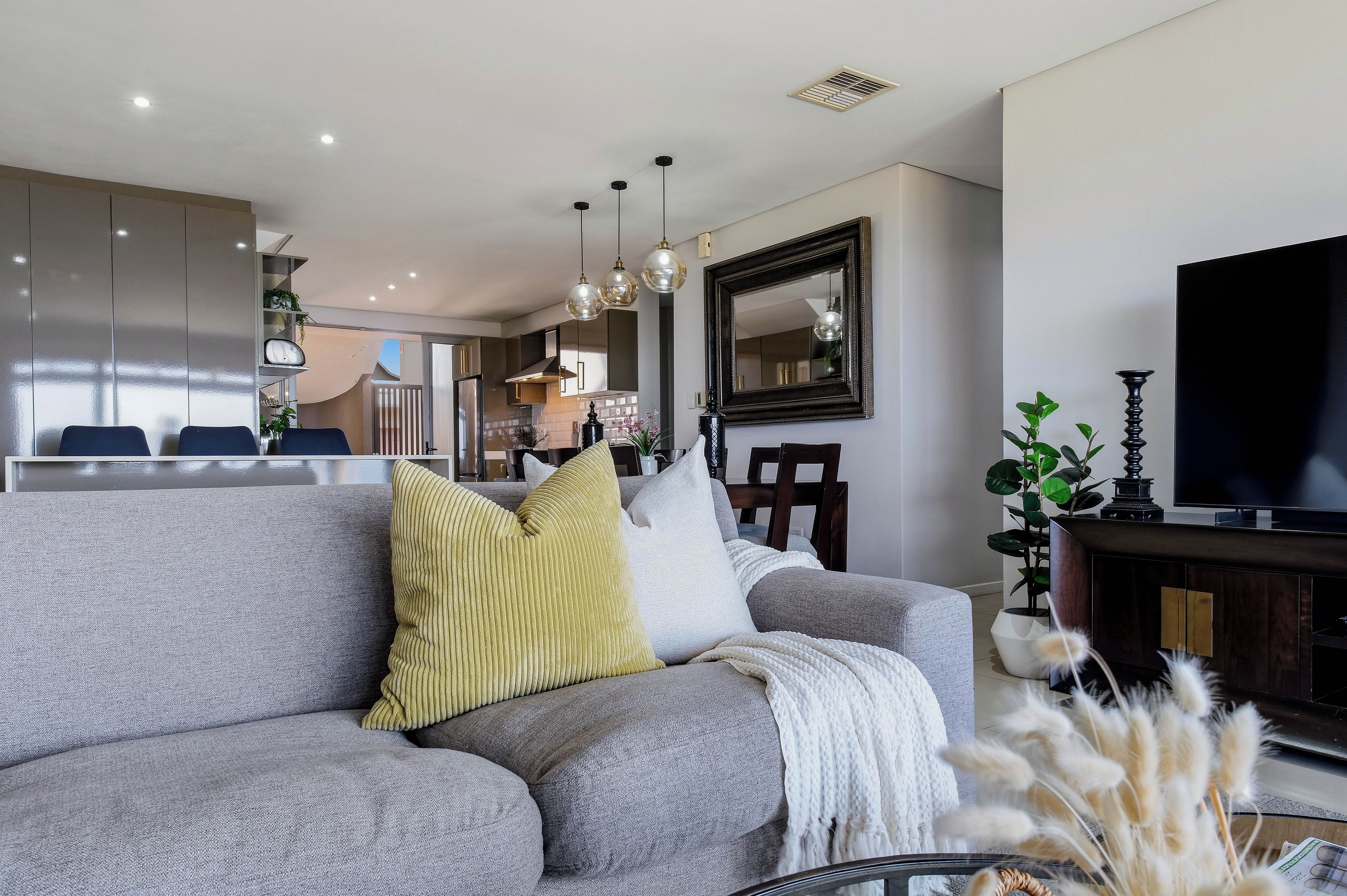 A modern living room with a grey sofa, a flat-screen TV, and a dining area in the background.