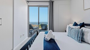 A hotel room with a bed, a view of the sea, and a balcony with chairs. - Simbithi Coastal Escape | Luxury with Ocean Views (Dolphin Coast)