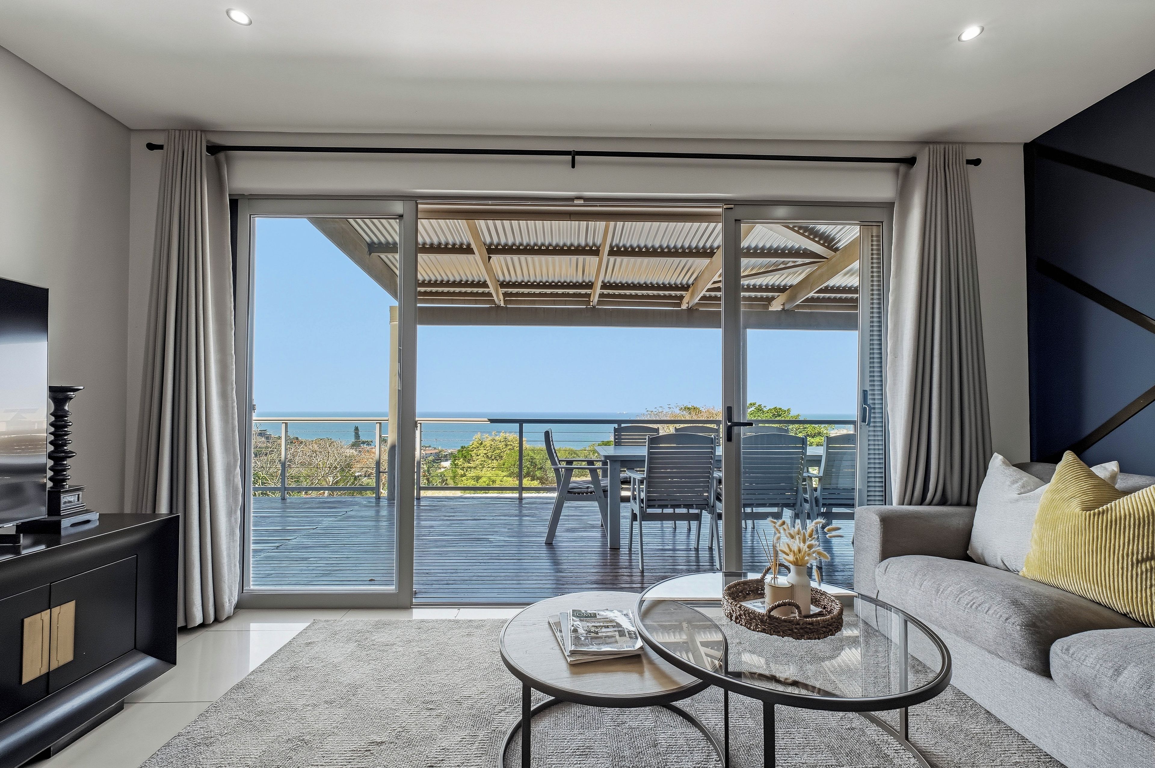 A modern living room with a large sliding glass door leading to a balcony with a view of the sea.