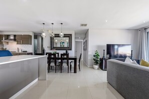 A modern living room with a grey sofa, a flat-screen TV, and a dining area with a table and chairs.