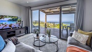 A modern living room with a large TV, two glass coffee tables, and a sofa with cushions.