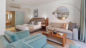 A hotel room with a bed, a sofa, a coffee table, a mirror, and a bathroom visible through a glass door. - Harbour Bridge Retreat | No Loadshedding (Cape Town)