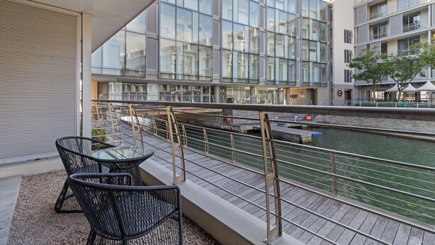 A modern building with large glass windows, a balcony with outdoor furniture, and a view of a river. - Harbour Bridge Retreat | No Loadshedding (Cape Town)