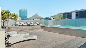 A rooftop pool area with lounge chairs, a pool, and a view of a mountain and a building in the background. - Harbour Bridge Retreat | No Loadshedding (Cape Town)