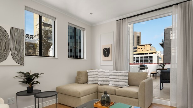A modern living room with a beige sofa, a glass coffee table, and a view of the city through large windows. - Venice-Inspired Penthouse with City Views (Cape Town)