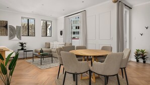A modern living room with a round wooden table, grey upholstered chairs, a sofa, and a coffee table. - Venice-Inspired Penthouse with City Views (Cape Town)